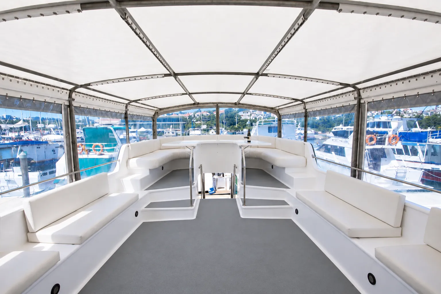 Covered top deck of Kiwa II with white bench seating, a central table and clear side panels looking out over the marina
